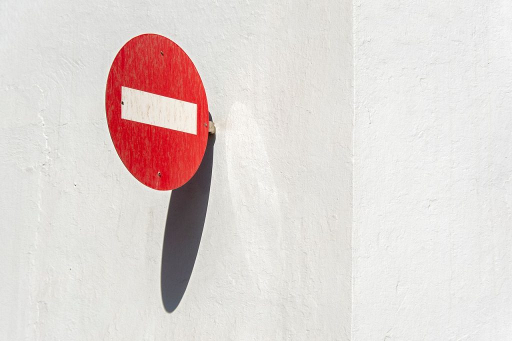 A minimalist photo of a red do not enter sign casting a shadow on a white wall.