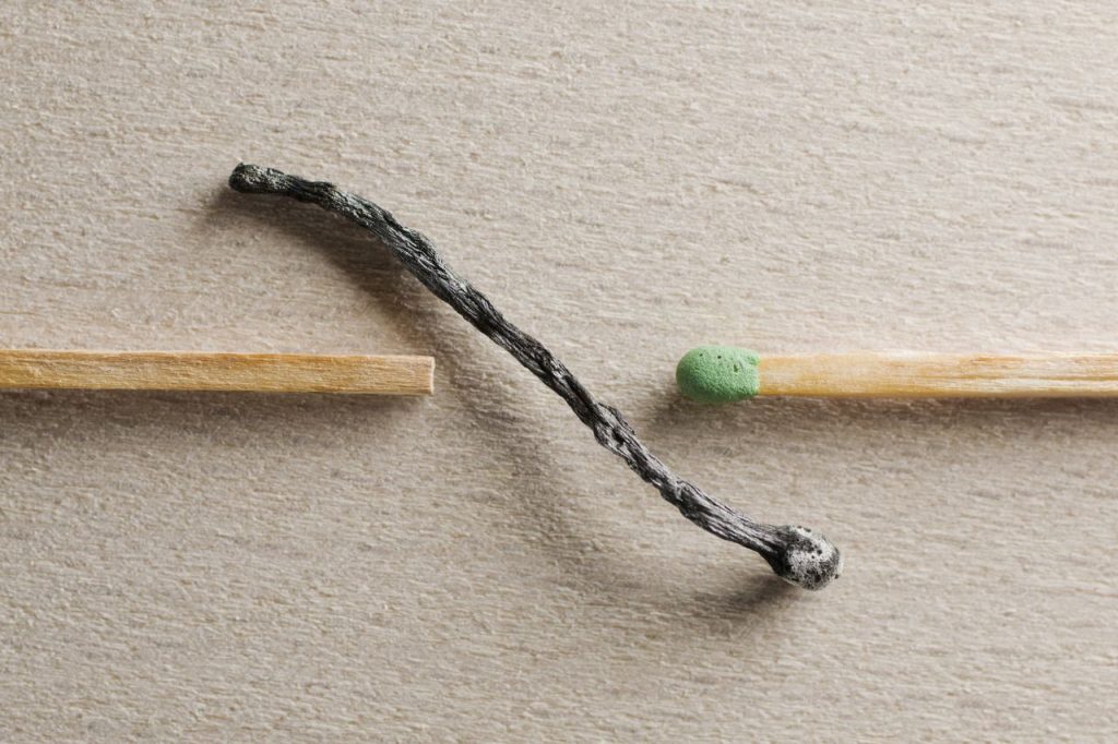 Artistic depiction of contrast between a burnt and unused match on a textured surface.
